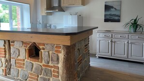 Une cuisine dotée d’un îlot central en pierre, de meubles blancs et offrant une vue sur l’extérieur.