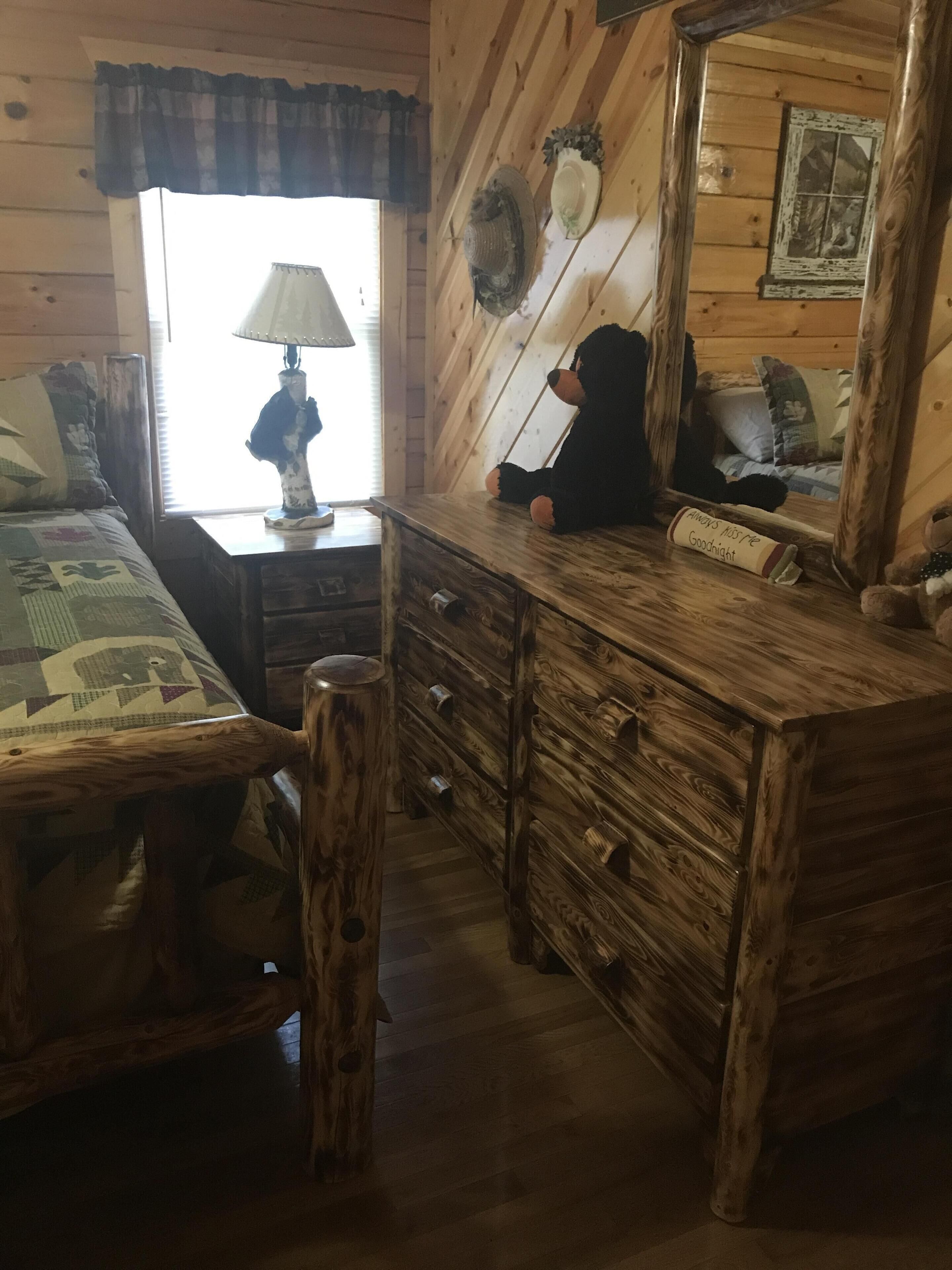 Une pièce de style cabane en bois, comprenant un lit, une commode, un miroir et une fenêtre avec des rideaux.