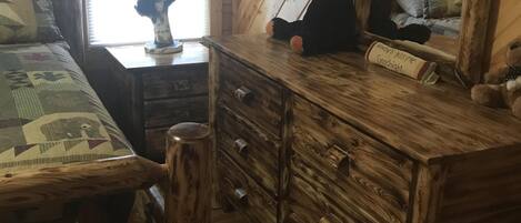 Une pièce de style cabane en bois, comprenant un lit, une commode, un miroir et une fenêtre avec des rideaux.