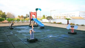 An outdoor playground with a blue slide, swings, and a seesaw.