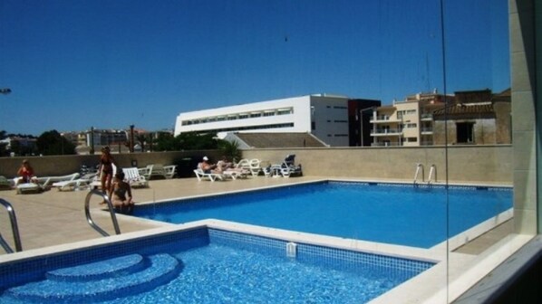 Una piscina con sillones de descanso y un edificio moderno al fondo.