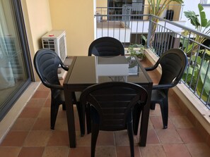 Un balcón con mesa y sillas, un equipo de aire acondicionado y vista al exterior del edificio.