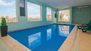 Ein Hallenbad mit klarem, blauen Wasser, großen Fenstern und einem gefliesten Boden.