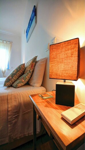 Un dormitorio con cama, almohadas, una mesita de noche con lámpara y un cuadro en la pared.