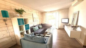 A living room with a sofa, coffee table, and a TV. There is a bookshelf and a plant. - 2 Bedroom apartment with swimming pool and underground parking (Grimaud)