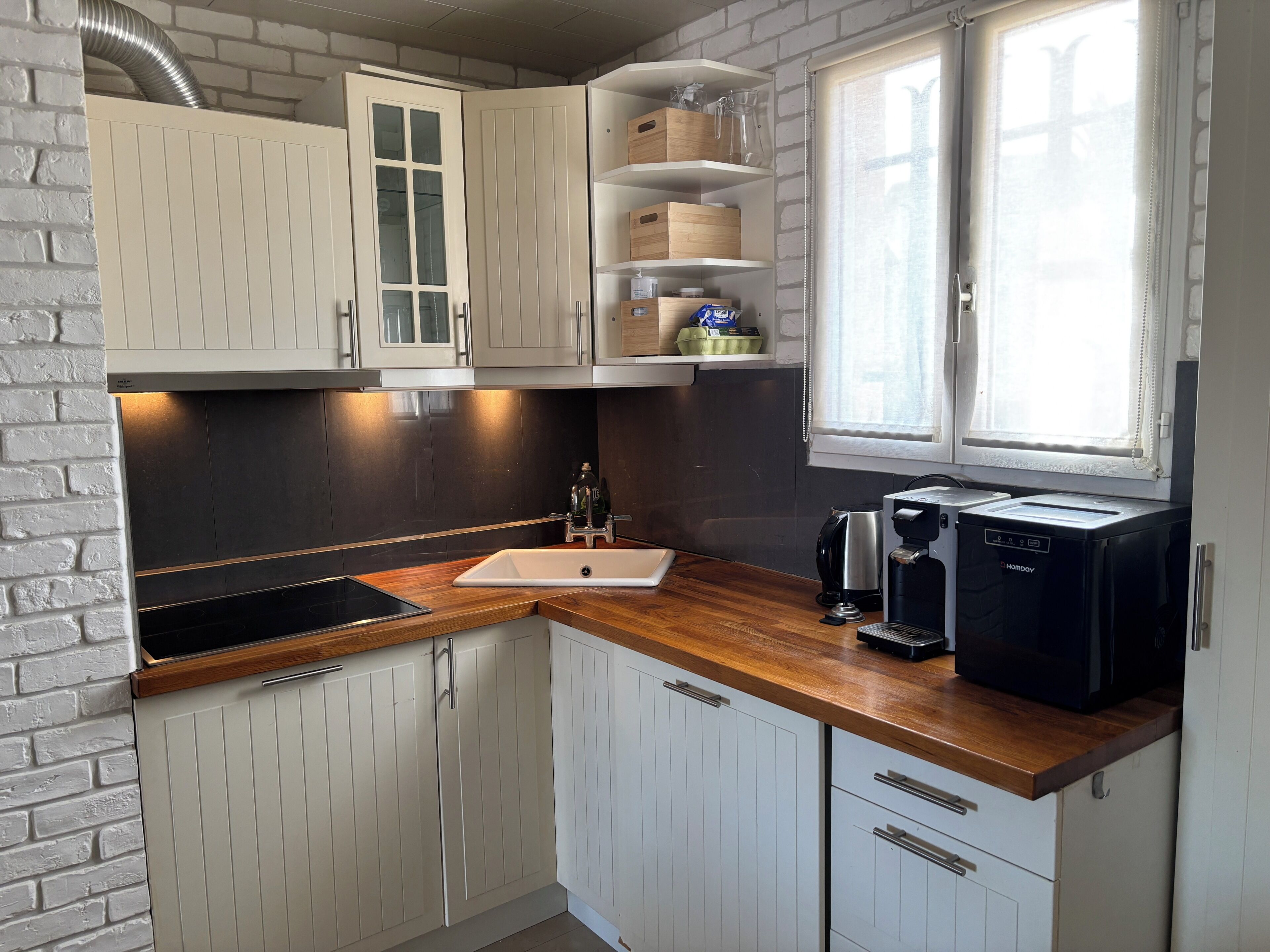 A kitchen with white cabinets, a wooden countertop, a sink, a coffee maker, and a window.