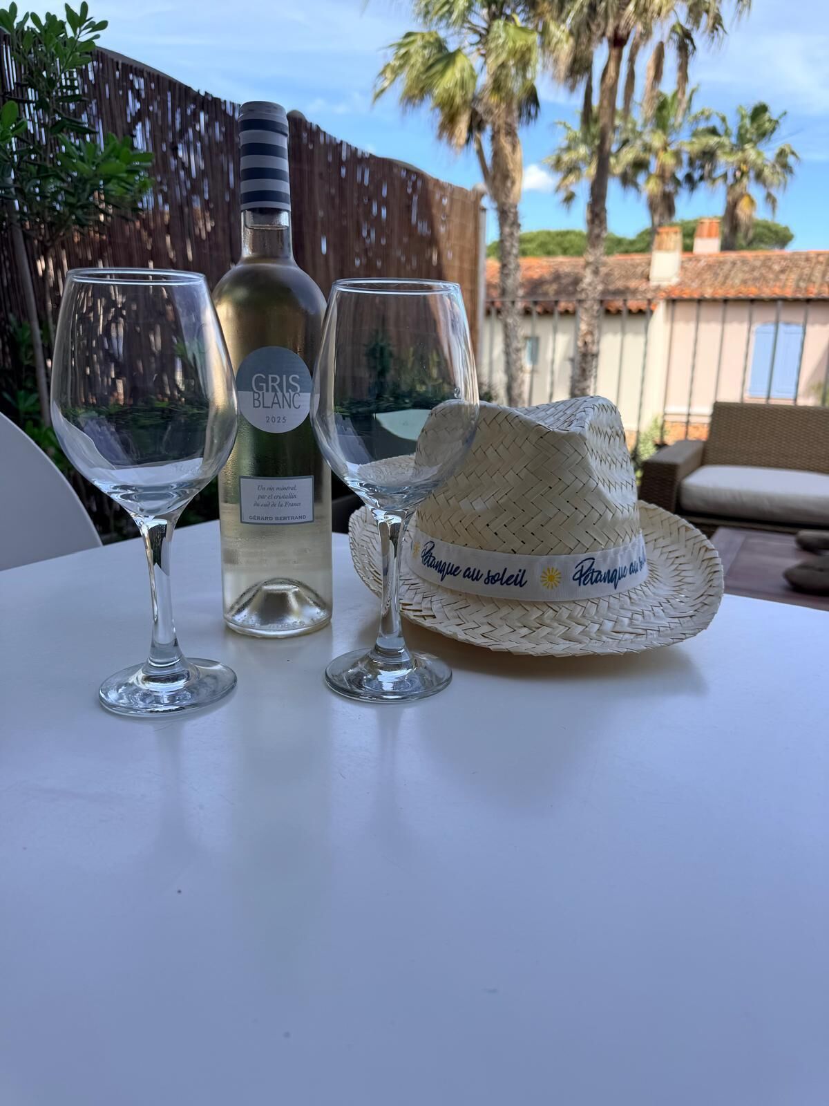 A table with two wine glasses, a bottle of wine, and a straw hat.