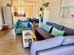 Un salon moderne avec un canapé bleu, un canapé gris et une table basse. Il y a également un coin cuisine équipé d’un réfrigérateur, d’un évier et d’une cuisinière.