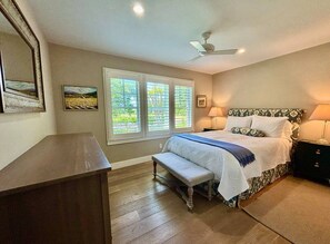 A bedroom with a bed, bench, nightstand, lamp, and a ceiling fan.