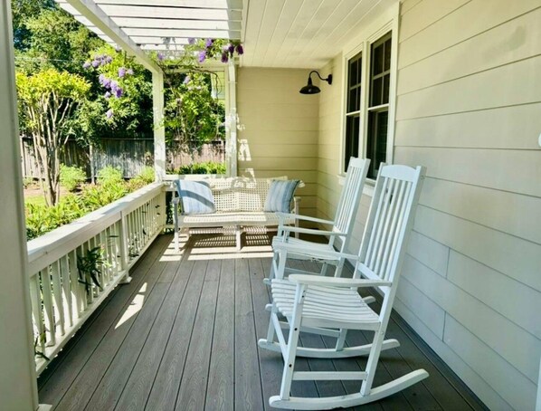 A porch with white rocking chairs, a covered area, and a wooden fence.