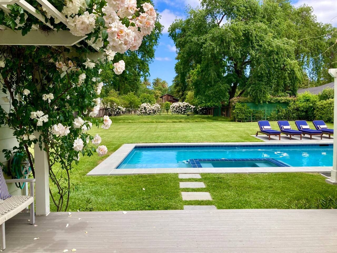 A swimming pool with a clear blue water surface, surrounded by a well-maintained lawn and a pergola with climbing plants.