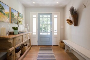 A hallway with a wooden bench, a blue door, wicker baskets, and a striped rug.