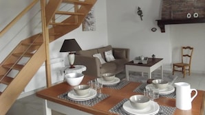 Un comedor con una mesa de madera dispuesta para cuatro personas, una escalera, un sofá y una pared de ladrillo.