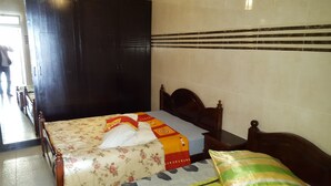 Ein Hotelzimmer mit Bett, Holz-Kopfteil, floralem Überwurf und gestreiftem Kopfkissen.