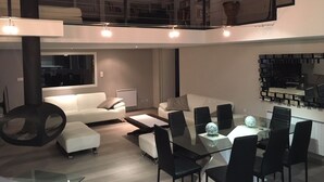 Een moderne woonkamer met een glazen eettafel, zwarte stoelen, een witte bank en een zwarte hangstoel.