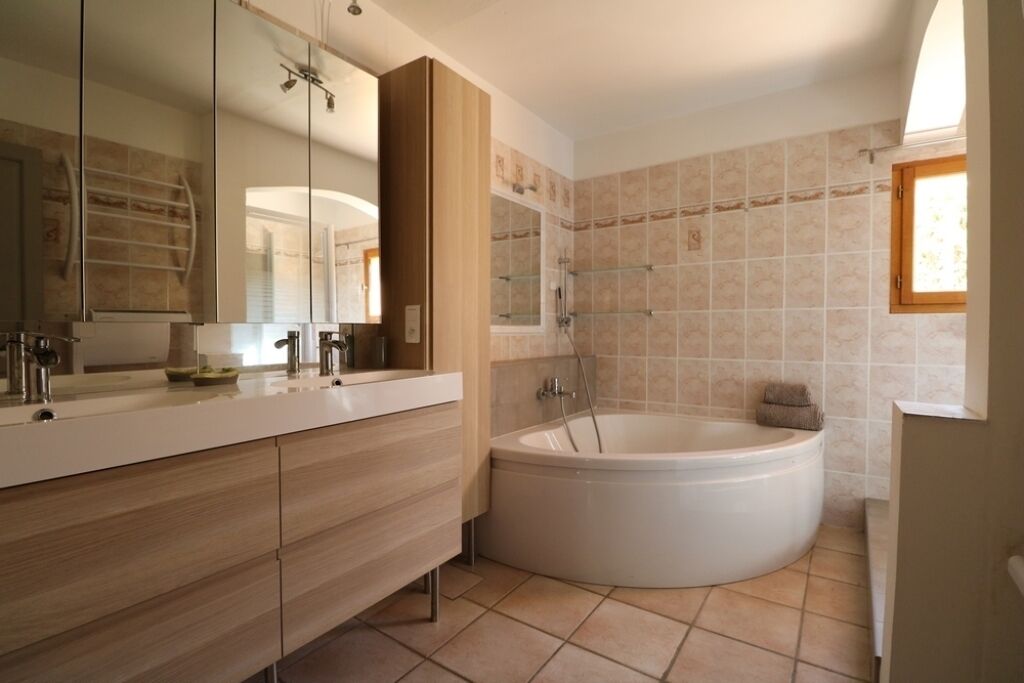 A modern bathroom with a large bathtub, a vanity with a mirror, and tiled walls.