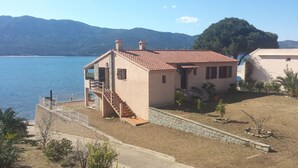 Una casa costera con techo de tejas rojas, una escalera de piedra y vistas al mar y a las montañas.