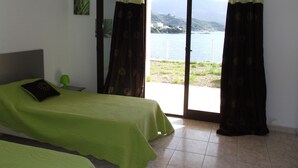 Un dormitorio con cama, mesita de noche y vista a un cuerpo de agua a través de una puerta corrediza.