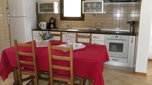 Cocina funcional con refrigerador, microondas, pileta y horno. Se aprecia una mesa de comedor con sillas y mantel rojo.