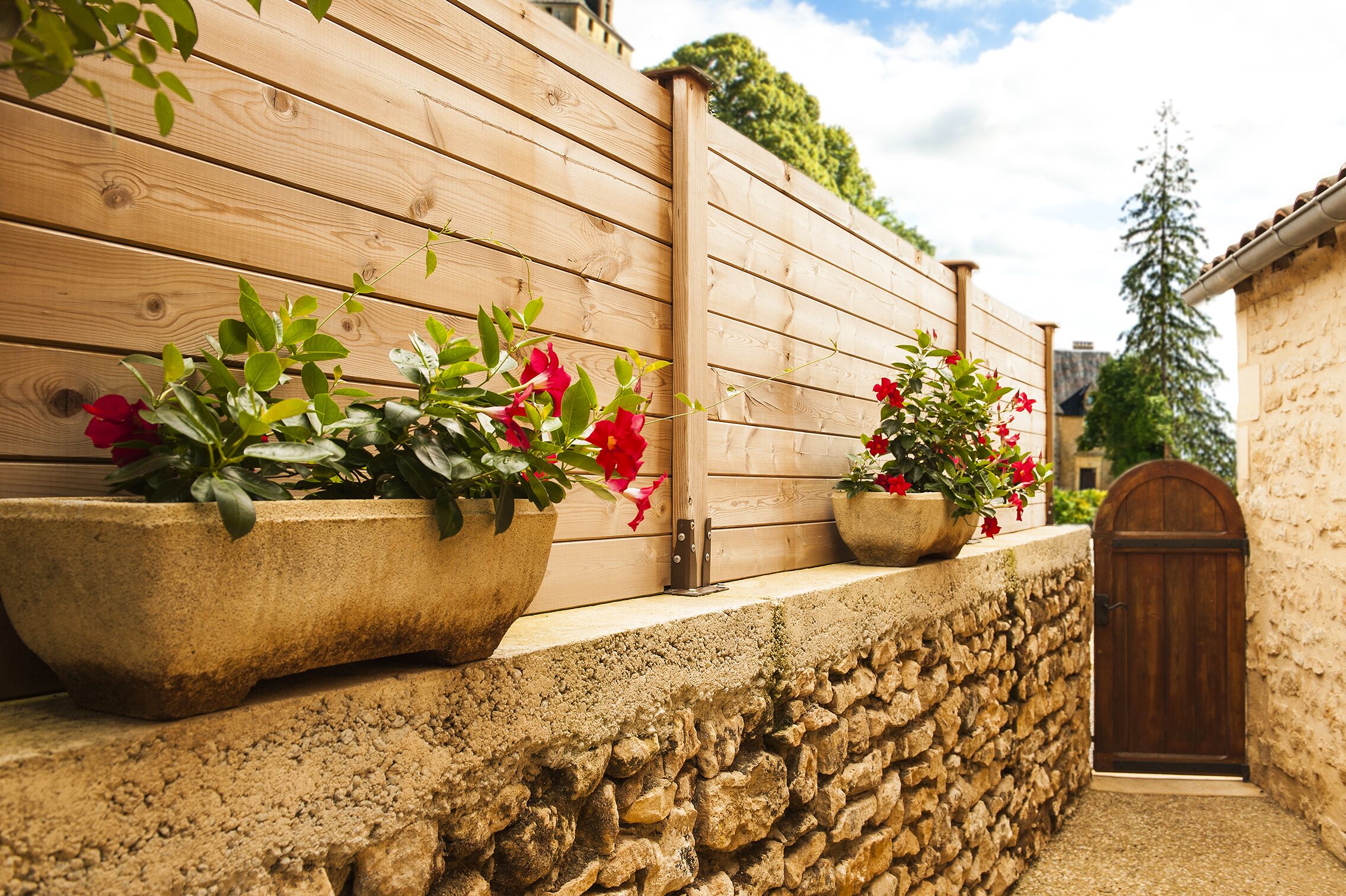 A stone wall with wooden planters containing red flowers.