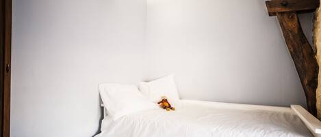 Quarto com cama branca, cabeceira de madeira e luminária fixa na parede.