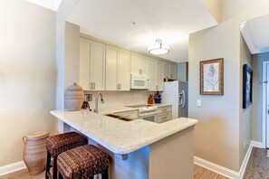 A kitchen with white cabinets, a marble countertop, and a built-in microwave. There are wicker stools and a basket on the floor.