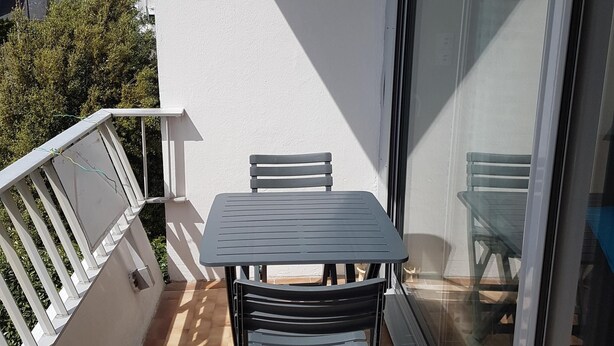 A balcony with a table and chairs, a sliding glass door, and a white railing. - TOWN CENTER QUIBERON (Quiberon)