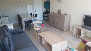 A modern living room with a sofa, a coffee table, a dining area with chairs, a TV on a stand, and a cabinet. - TOWN CENTER QUIBERON (Quiberon)
