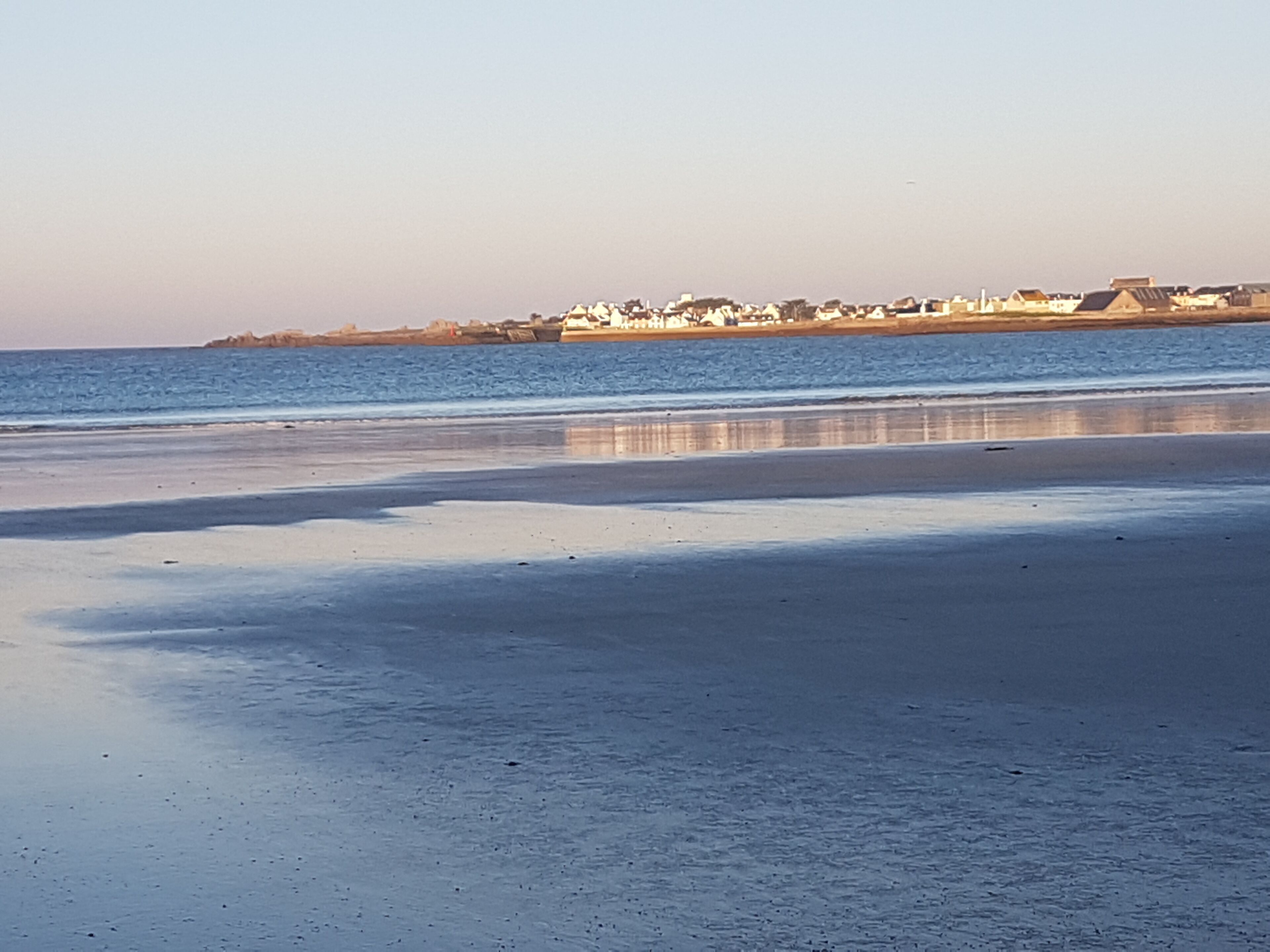 A beach with a calm sea and a distant shoreline with buildings.