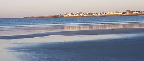 A beach with a calm sea and a distant shoreline with buildings.