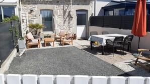 A stone house with a patio area featuring outdoor furniture and a table. - Little corner of paradise 2 steps from the sea. Walled garden. Wireless (Loctudy)