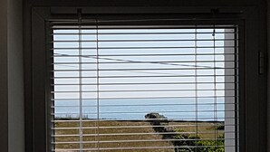 A window with horizontal blinds, a view of a road, and a distant landscape. - Little corner of paradise 2 steps from the sea. Walled garden. Wireless (Loctudy)
