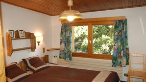 Une chambre à coucher avec un grand lit, une tête de lit en bois, une fenêtre avec des rideaux, une lampe de chevet et une étagère avec des photos.
