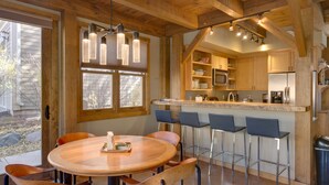 A modern kitchen with wooden beams, a central island with bar stools, and a dining area with a round table and chairs. - Downtown Durango-New Custom Timber Frame-the Carriage House (Durango)