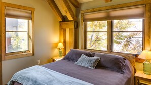 A bedroom with a large bed, two bedside lamps, and a window with a view of trees. - Downtown Durango-New Custom Timber Frame-the Carriage House (Durango)