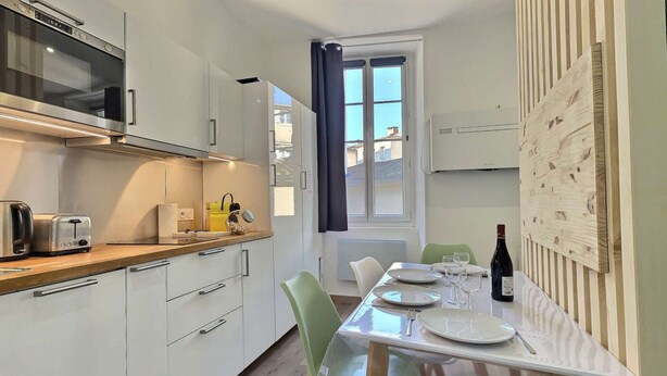 A modern kitchen with a built-in oven, a dining table set with plates and glasses, and a bottle of wine.