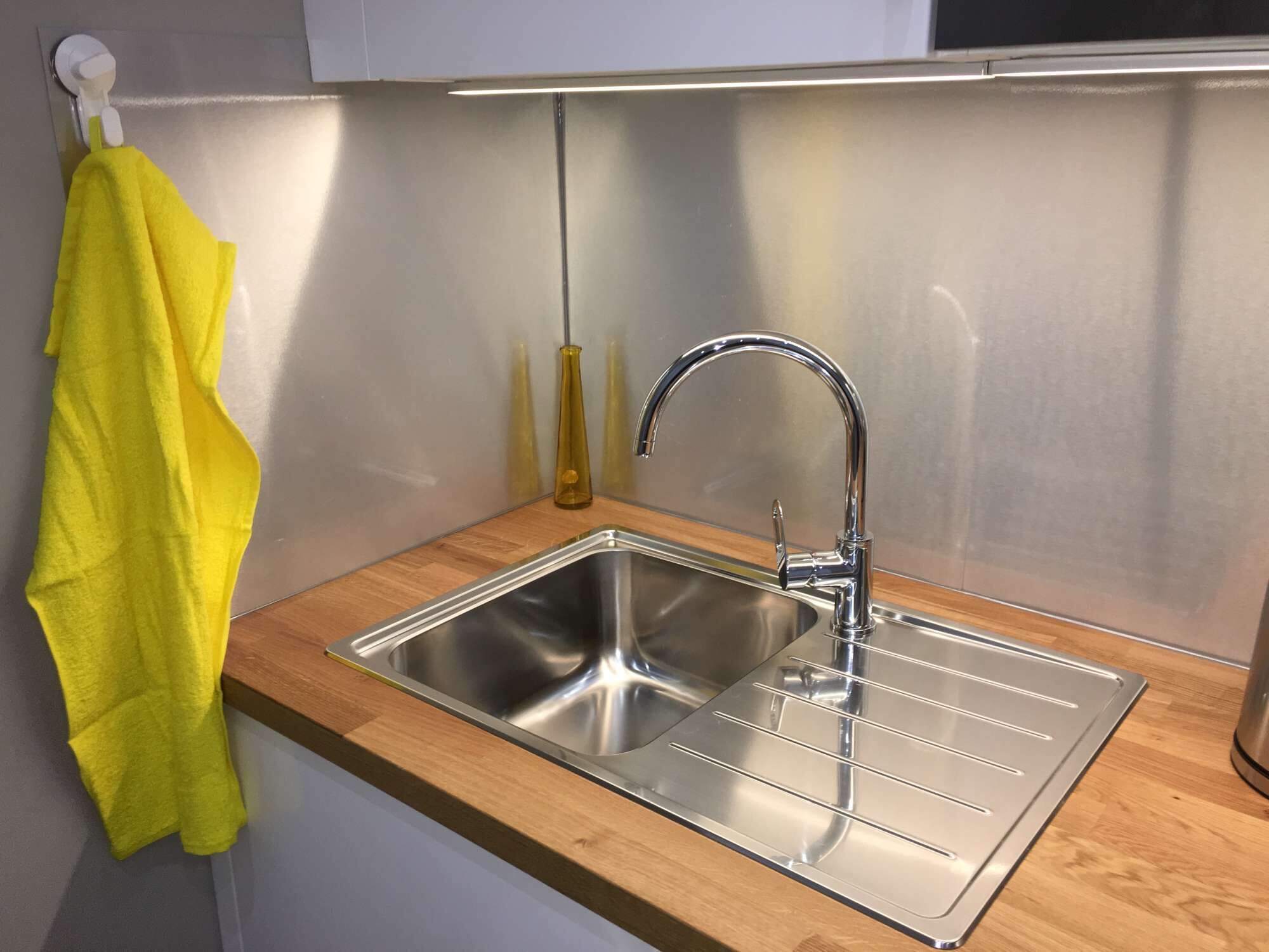 Ett modernt kök med en diskho i rostfritt stål, en bänkskiva i trä och en gul handduk som hänger på en krok.