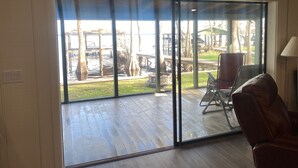 A room with a large sliding glass door leading to a deck with a view of a lake and dock.