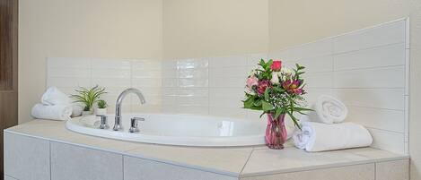 A modern bathroom with a large bathtub, a sink, and a vase of flowers.