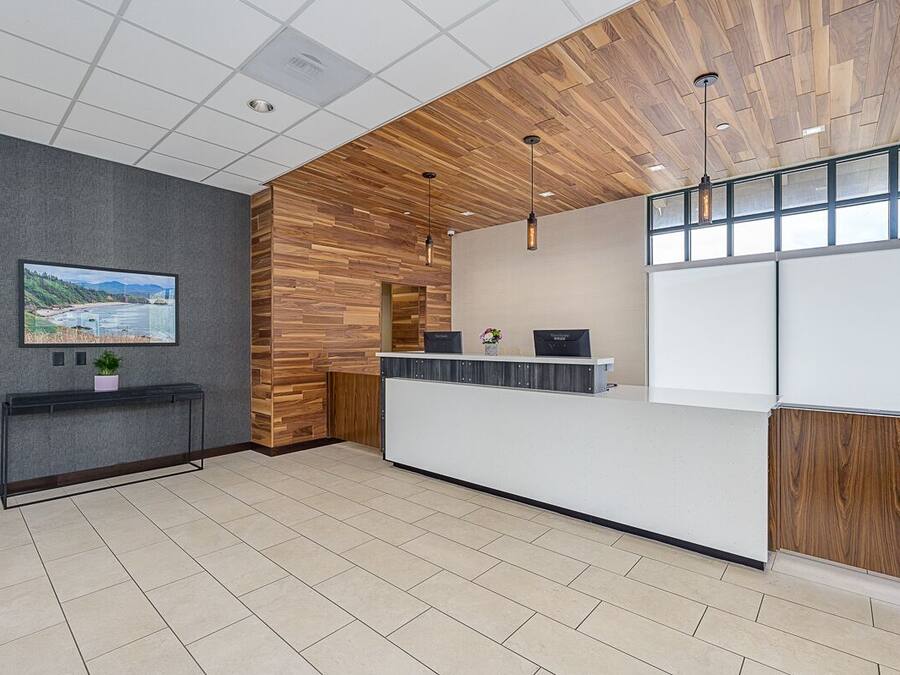 Un área de recepción con techo de madera, una pared gris con un cuadro enmarcado, un mostrador de recepción y piso de baldosas.