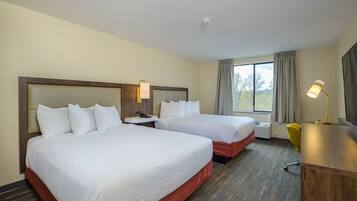 A hotel room with two beds, a desk, a lamp, and a window with curtains.