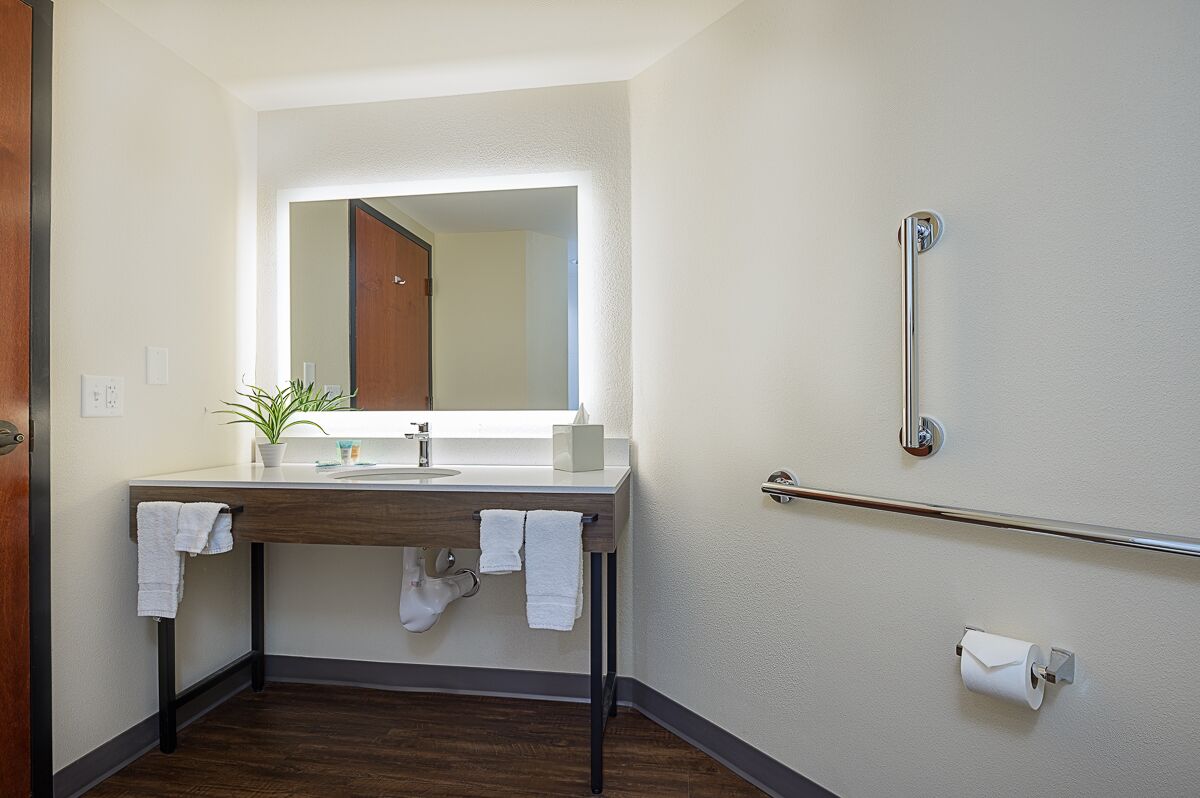A modern bathroom with a wooden vanity, a mirror, a towel rack, and a handrail.