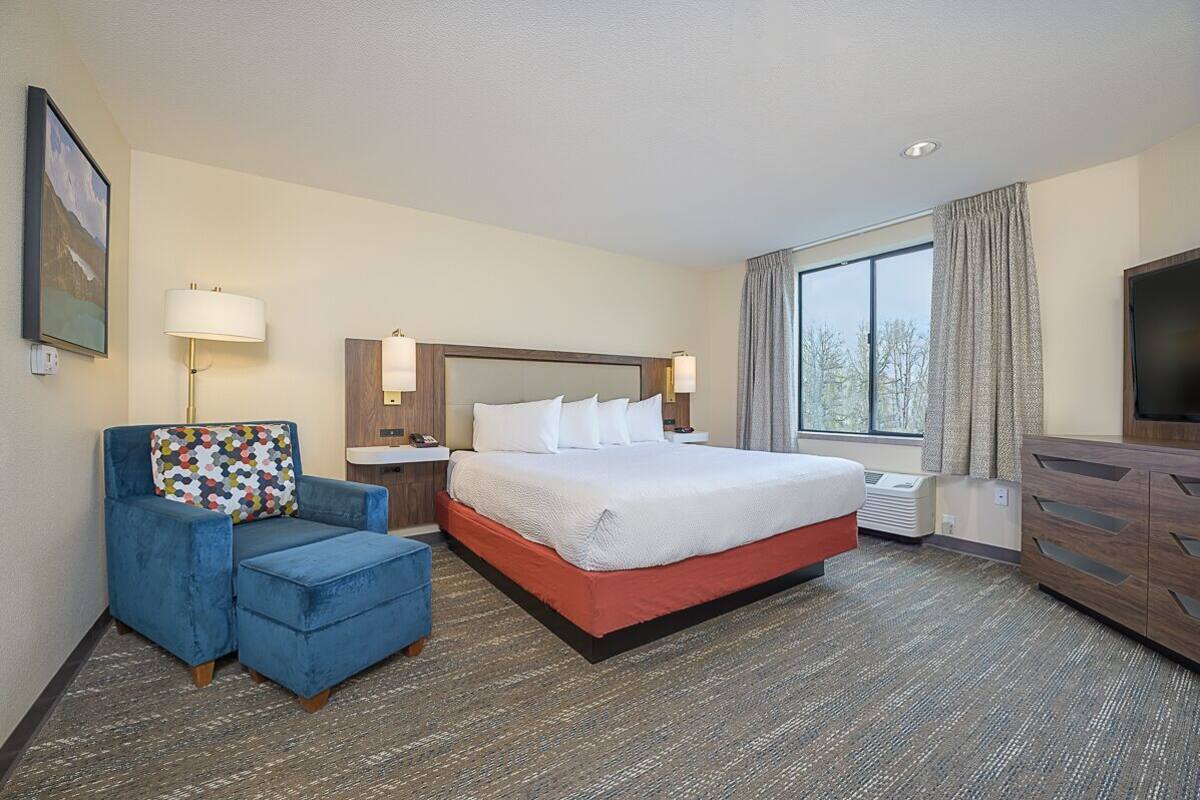 A hotel room with a large bed, a blue armchair, a desk with a lamp, and a TV.