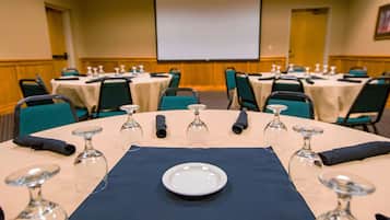 Une salle de conférence avec des tables rondes disposées pour les réunions, équipée de verres à vin et d’assiettes.