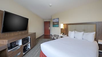 A hotel room with a large bed, a flat-screen TV mounted on a wooden cabinet, a small table with a lamp, and a painting on the wall.