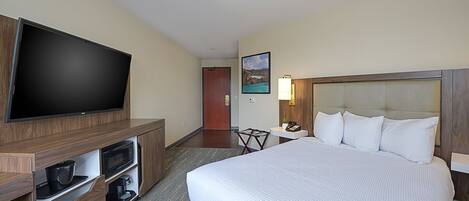 A hotel room with a large bed, a flat-screen TV mounted on a wooden cabinet, a small table with a lamp, and a painting on the wall.