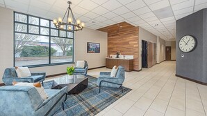 A spacious lobby with a modern design, featuring a seating area with sofas and a coffee table, a large window offering a view of the outdoors, a wooden accent wall, and a clock on the wall. - Portlander Inn and Marketplace (Portland)