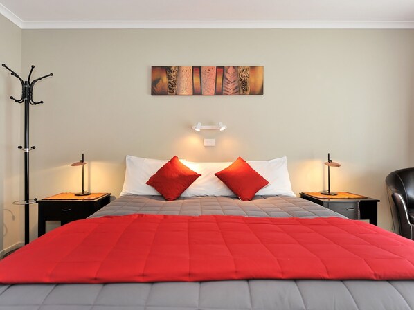 A hotel room with a bed, two red pillows, a red blanket, a wall art piece, and two bedside lamps. - Mohua Motels (Takaka)