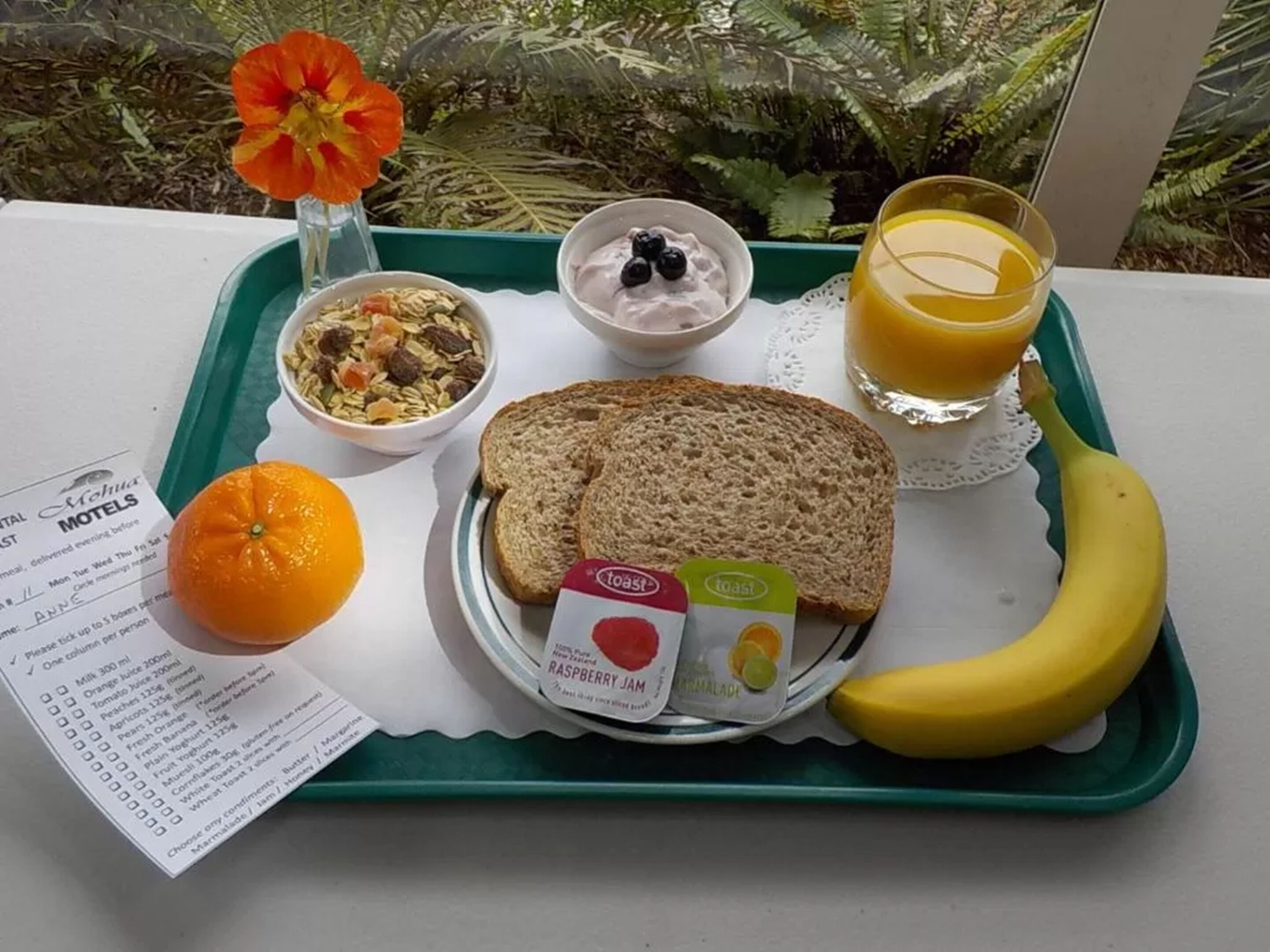 Un plateau de petit-déjeuner avec des toasts, du yaourt, une orange, une banane et du jus de fruits.