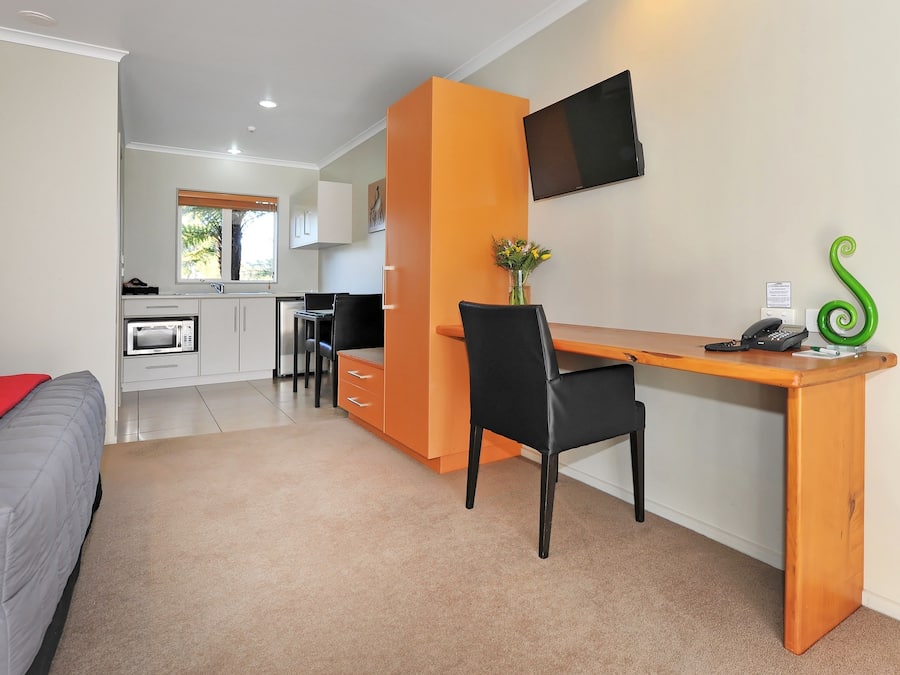 Una habitación de hotel compacta con kitchenette, un escritorio y una silla, y una cama.